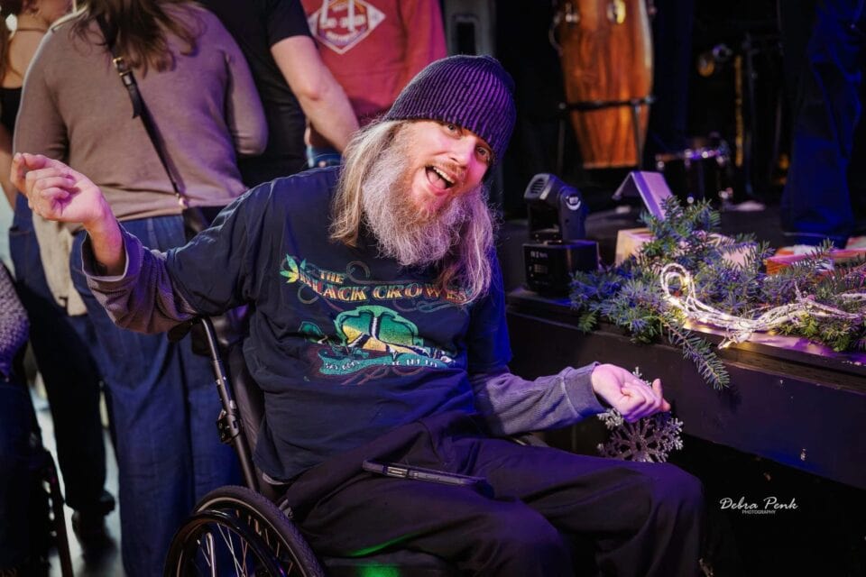 Johnny Wheels making a smiling jovial gesture to the camera while at the holiday themed merchandise table.
