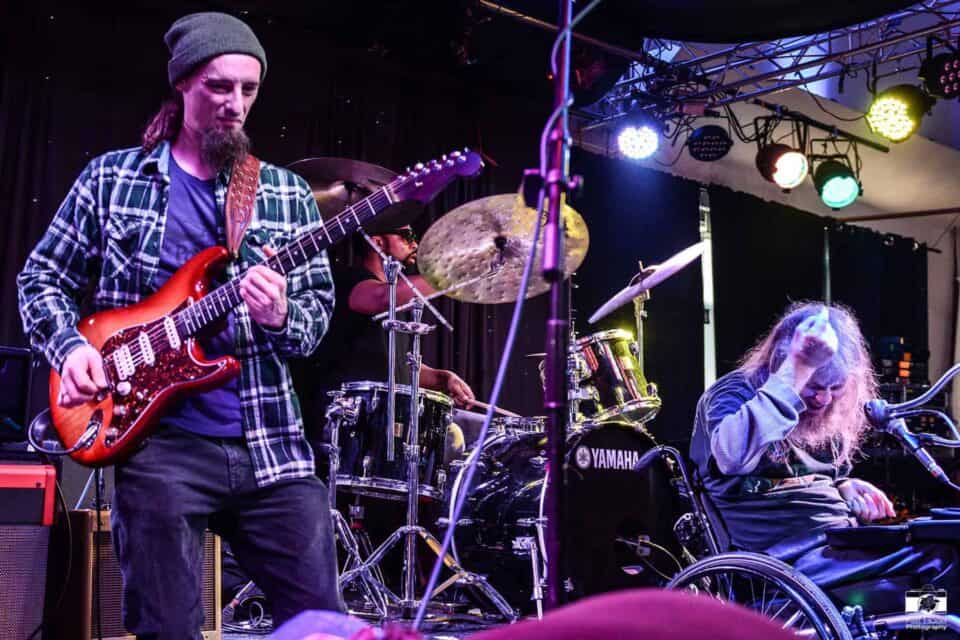 Brandon playing a guitar solo with Johnny and the drummer in the background.