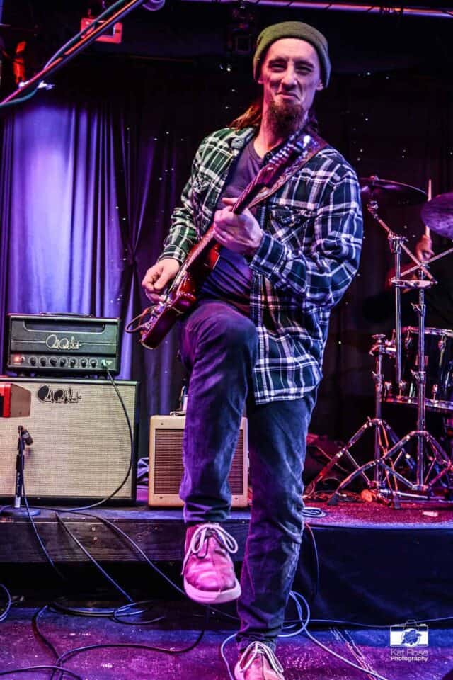 Brandon Logan having a good time high-steppin' while playing on stage and looking at the camera.