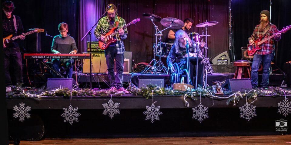 Johnny Wheels & The Swamp Donkeys on stage during the holidays - the stage is dressed with green garland at the front of the stage with large star ornaments hanging over the front.