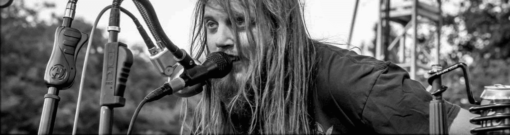 Picture of Johnny Wheels singing on stage (in his wheelchair) at an outdoor festival.