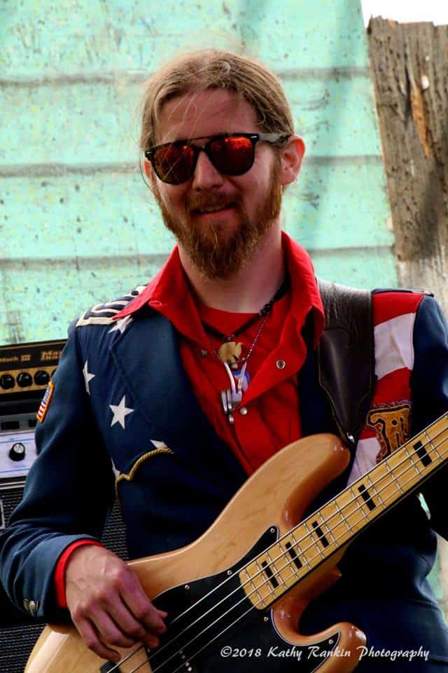 Picture of Taylor Frazier playing his guitar, with his saxophone sitting on a stand in front of him, on stage at the Journey To Memphis band competition - at the Portland Blues Festival, at the Portland Oregon Waterfront.